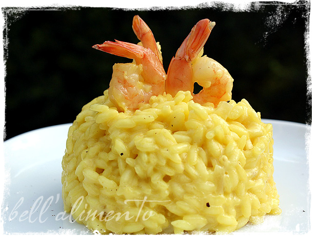 White plate with scoop of saffron risotto topped with standing cooked shrimp for presentation. 