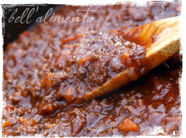 close up of wooden spoon in meat sauce. 