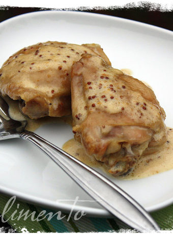 chicken thighs with mustard sauce on white plate with fork. Striped napkin under plate.
