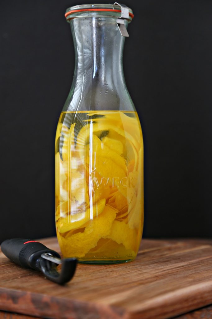Glass carafe with lemon peels inside and liquid. Vegetable peeler in front of carafe. 