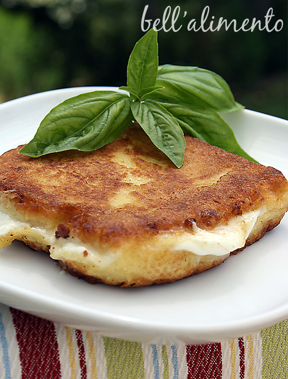 Italian grilled cheese on white plate garnished with fresh basil. 