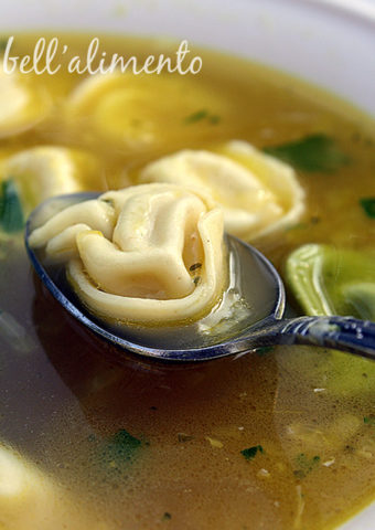 closeup of tortellini soup in bowl. Spoon with tortellini in bowl.