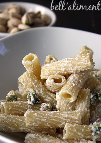 White bowl of Maccheroni alla Ricotta (Macaroni with Ricotta) pasta. Small white bowl of pistachios in background.