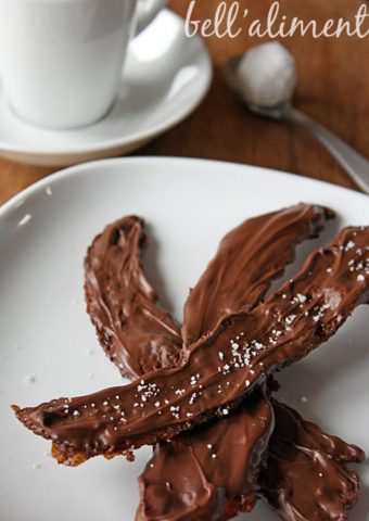 Nutella Covered Bacon on white plate with coffee cup, saucer and spoon behind.