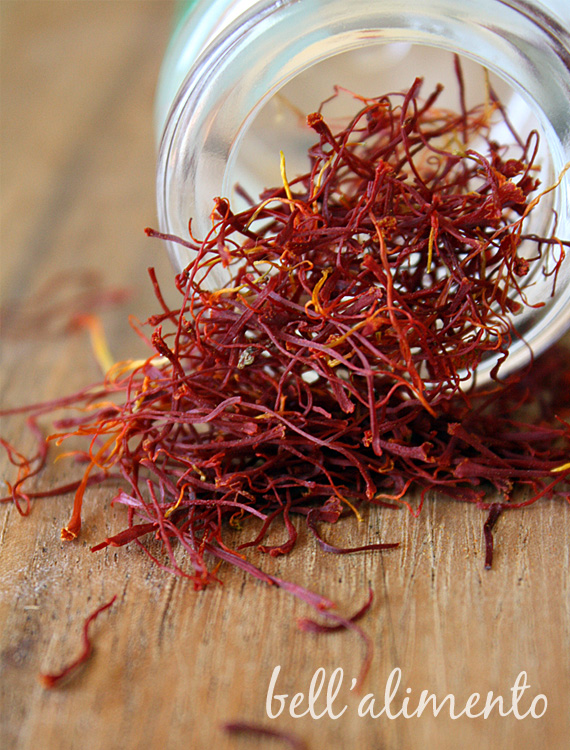 Small glass jar of Saffron on side with saffron threads spilling out. 