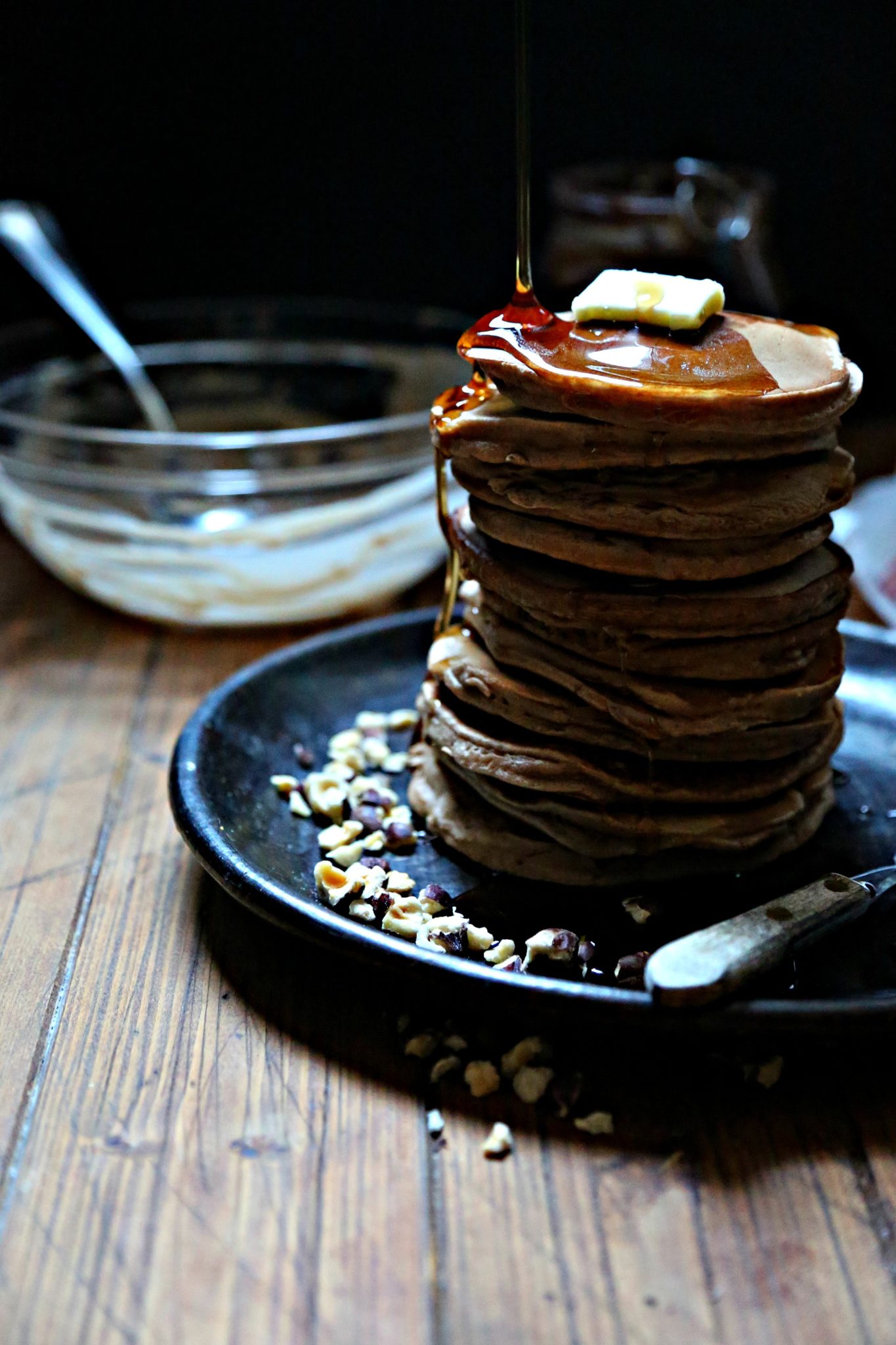 Stack of nutella pancakes with butter and syrup with messy bowl behind