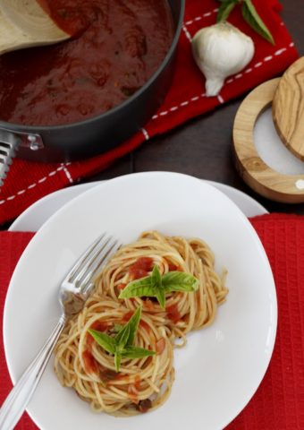 Spaghetti with Salsa di Pomodoro - Tomato Sauce on white plate. Pot of sauce on red kitchen towel behind. Salt cellar to side.