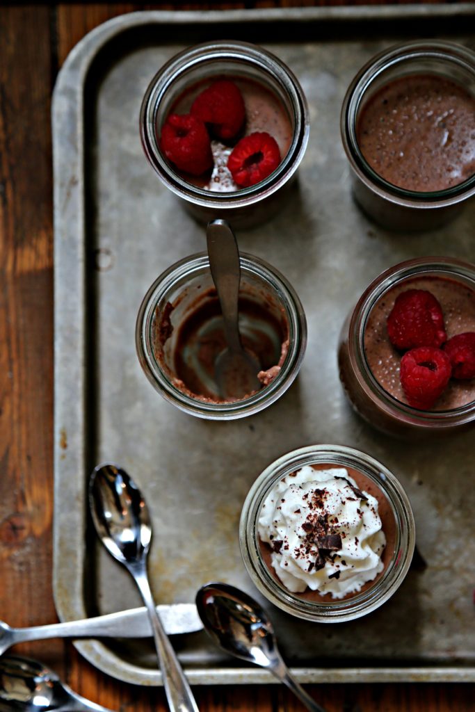 Chocolate Amaretto Panna Cotta in small glass jars. Garnished with raspberries, whipped cream and chocolate shavings, small spoons to side.