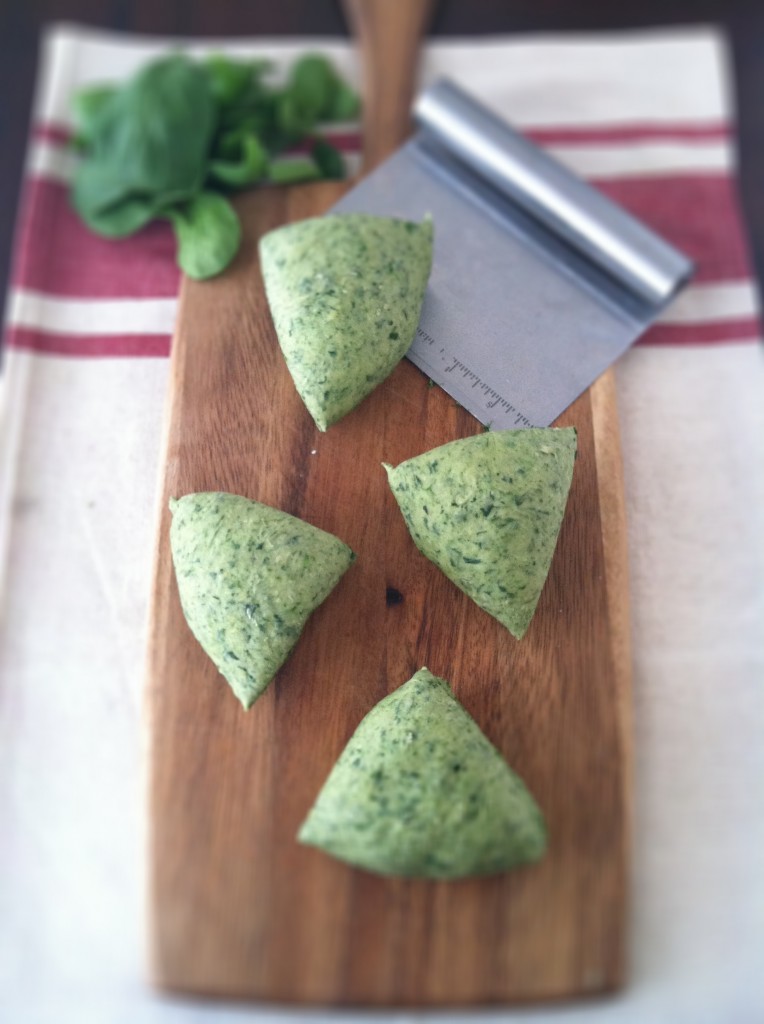 homemade spinach pasta dough on a wooden board with fresh spinach and pastry cutter