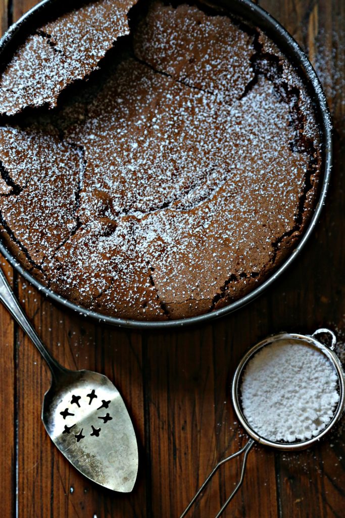 Chocolate cake with powdered sugar sifter and serving piece to side.