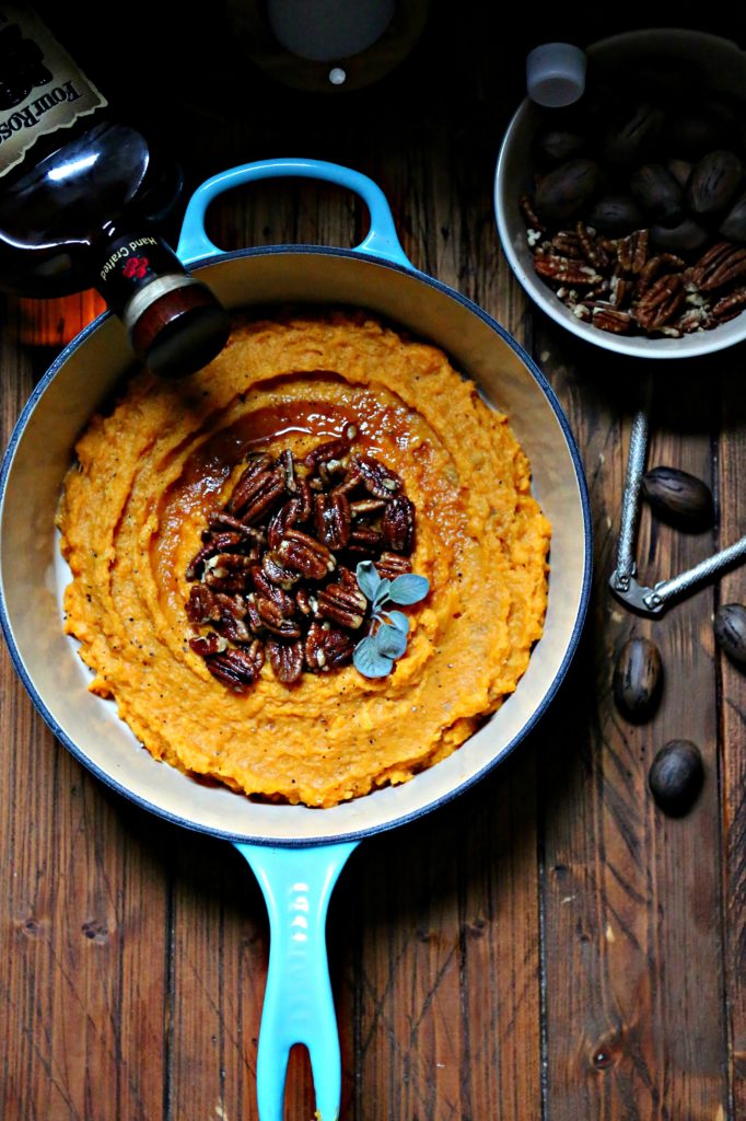 Boozy Smashed Sweet Potatoes in blue pot with bowl of pecans to side