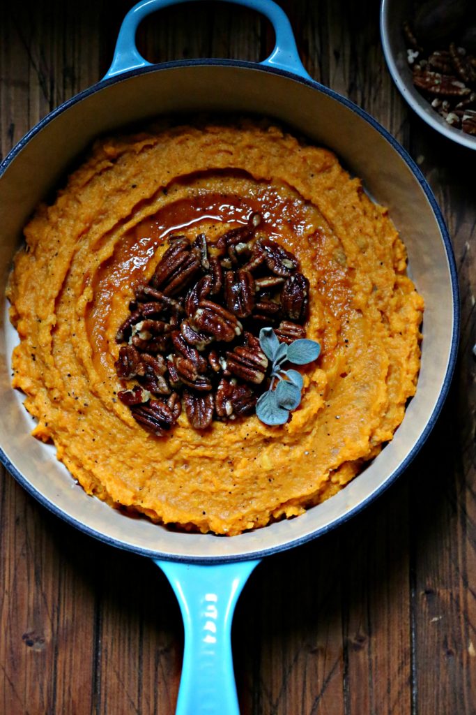 Boozy Smashed Sweet Potatoes in blue pot topped with pecans and sage