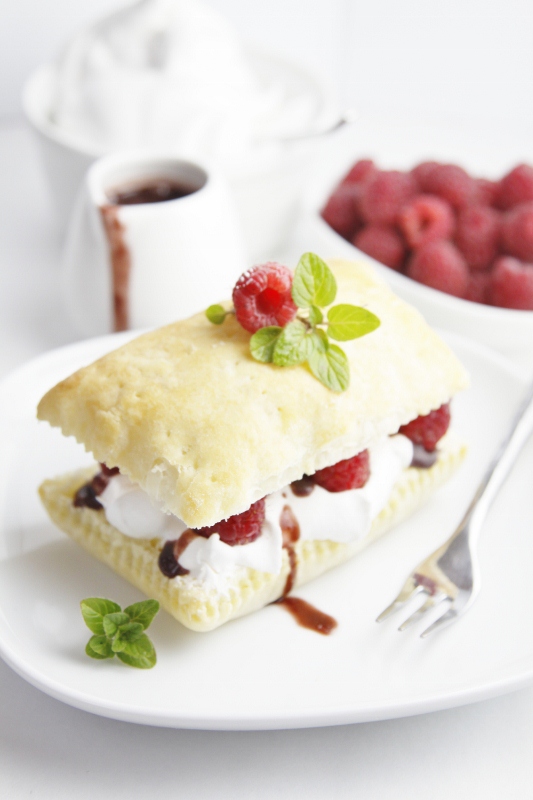 Raspberry Chocolate Napoleons on white plate with fork. Small pitcher of sauce and bowl of berries in background.