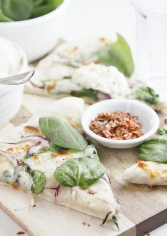 slices of spinach and ricotta pizza. Small white bowl of red pepper flakes in between.