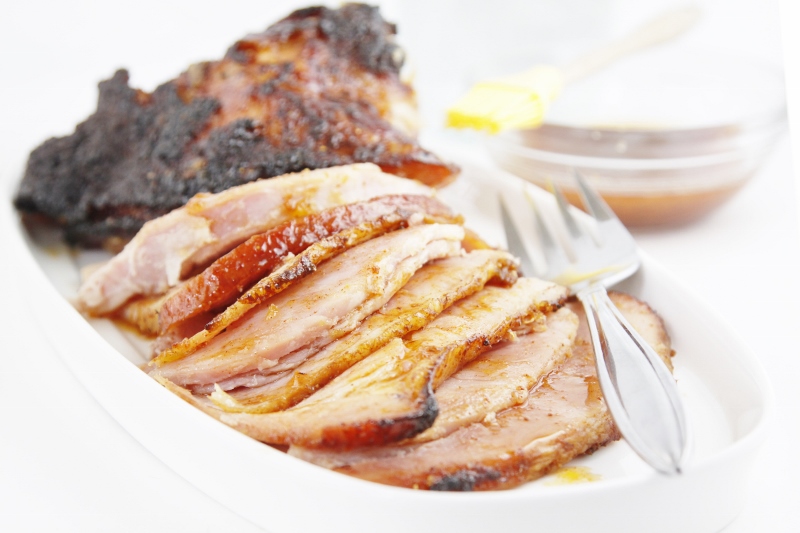 sliced glazed ham on a white serving tray with fork. 