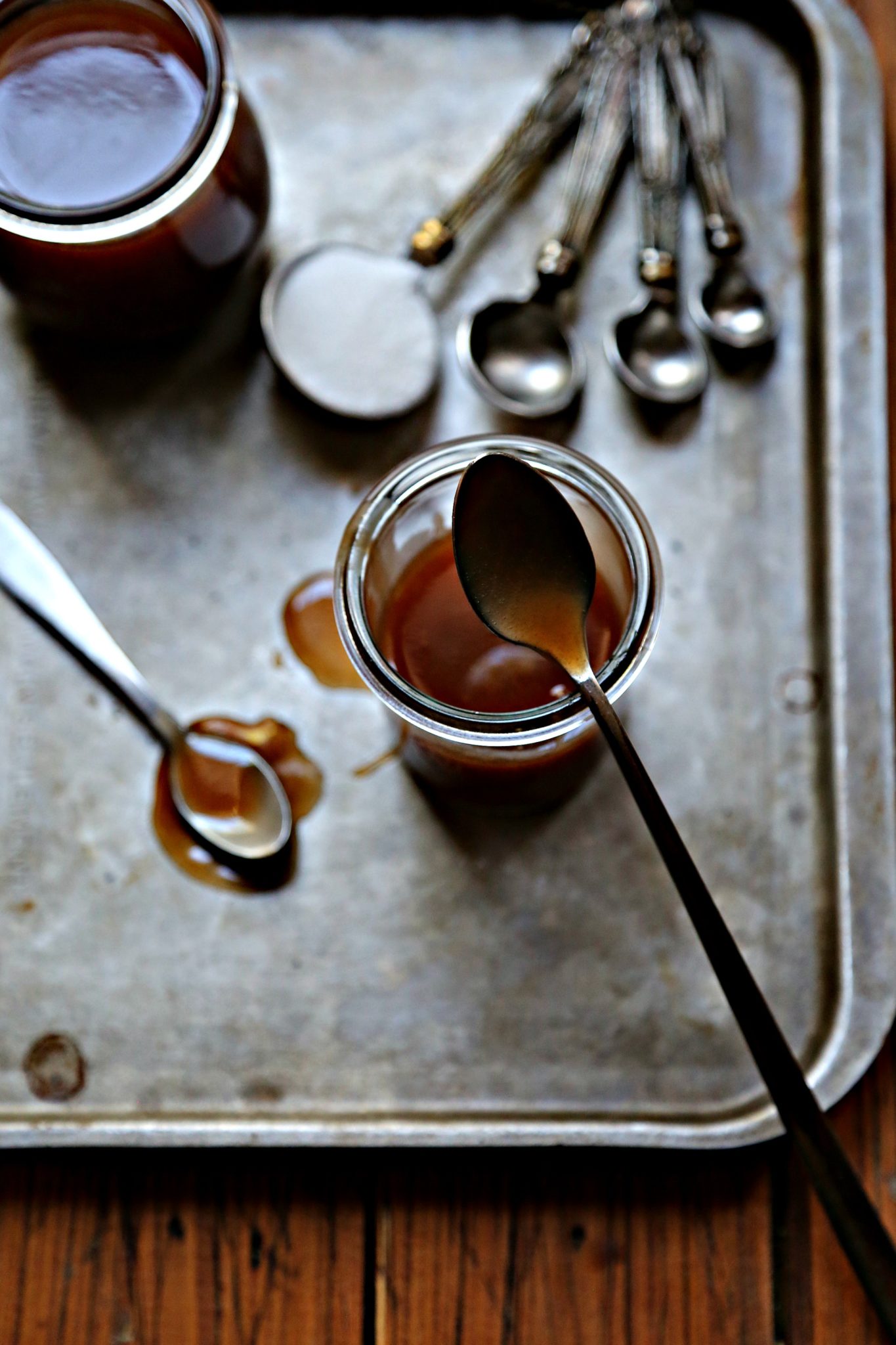 small jars of caramel sauce on baking sheet with spoons