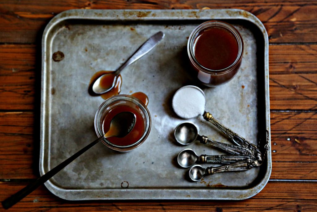 small jars of caramel sauce on baking sheet with spoons
