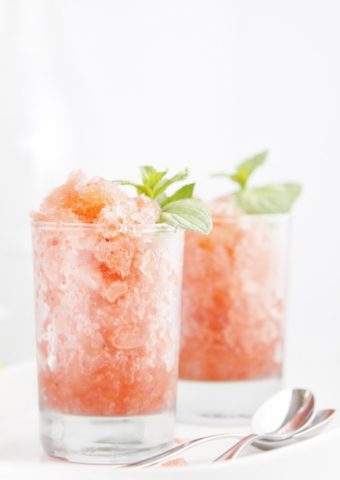 two glasses of boozy berry granitas garnished with fresh mint. Spoons to right.