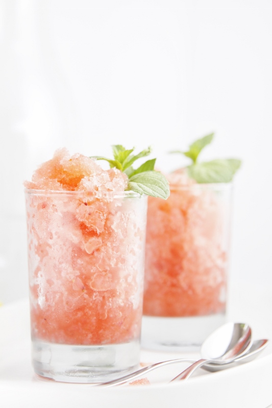 2 glasses of Boozy Berry Granitas garnished with mint with spoons to right. 