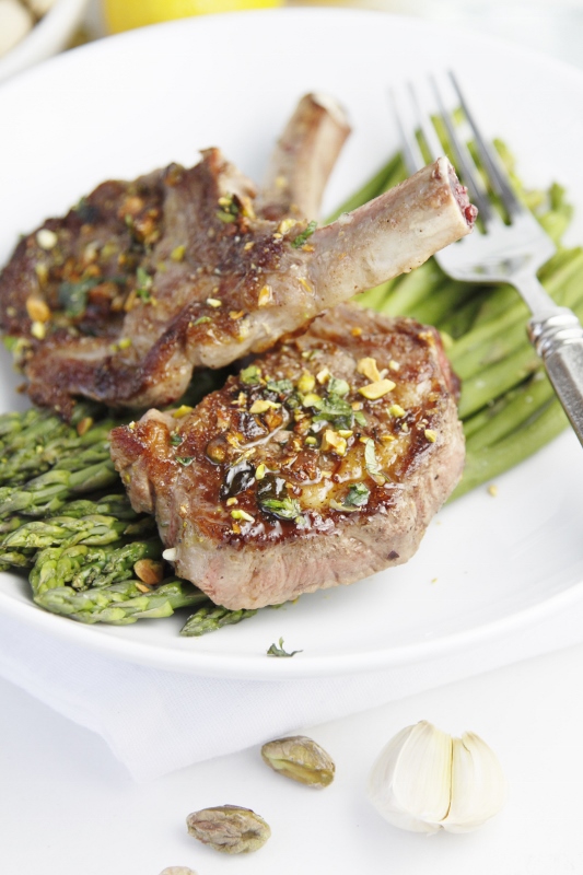 2 lamb chops sitting on top of a bed of asparagus with fork to side.