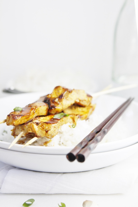 Chicken Yakitori skewers over Rice in white bowl. Chop sticks to side. 