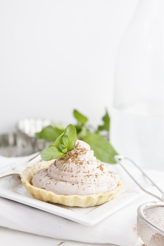 Mini tart filled with mousse on white plate with fork. Empty tart pans and fresh mint in background. 
