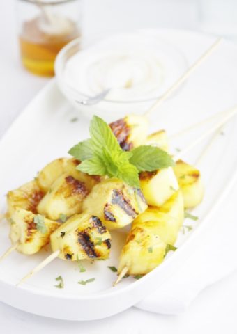 Pina Colada Grilled Pineapple Skewers on white plate with glass bowl of sauce.