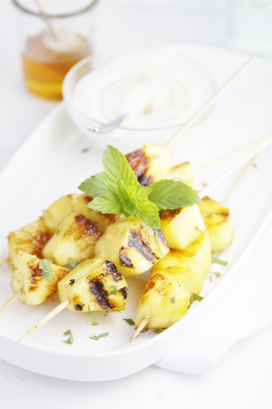 Pina Colada Grilled Pineapple Skewers on white tray with small glass bowl of yogurt with spoon. 