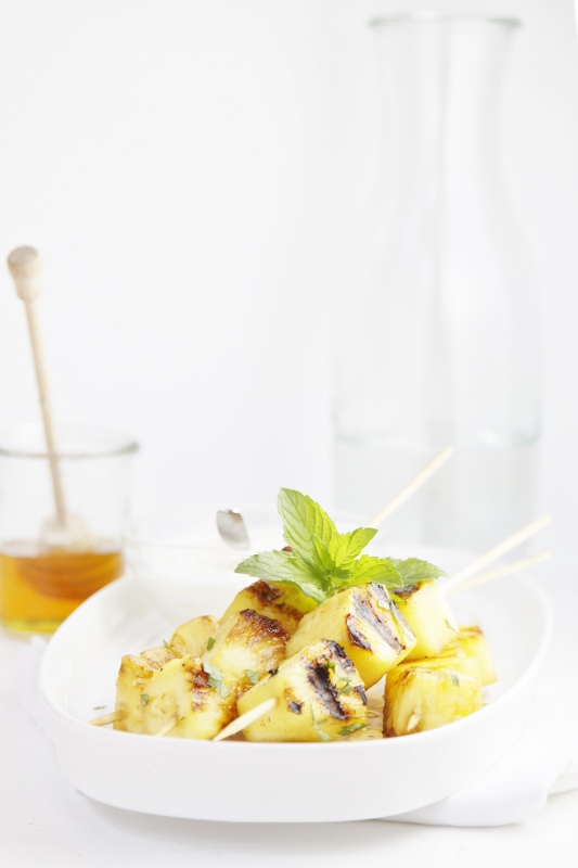 Pina Colada Grilled Pineapple Skewers on white tray. Small glass jar of honey in background.