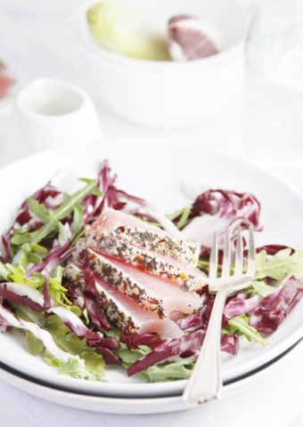 Sesame Seared Ahi Tuna Salad on white plate. Fork to Right. Small white pitcher of dressing in background.