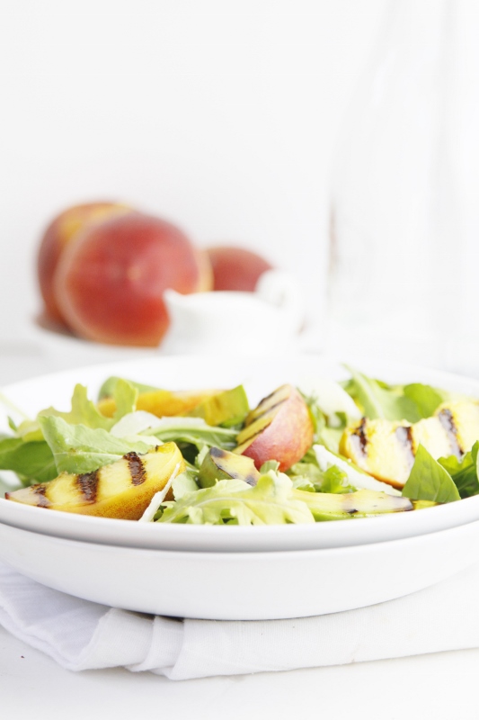 Grilled Peach and Avocado Summer Salad in white bowl. Peaches and glass carafe in background.