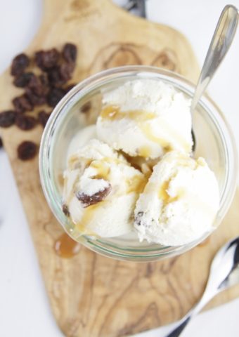 Rum raisin ice cream in glass jar on cutting board. Raisins to side along with a spoon.