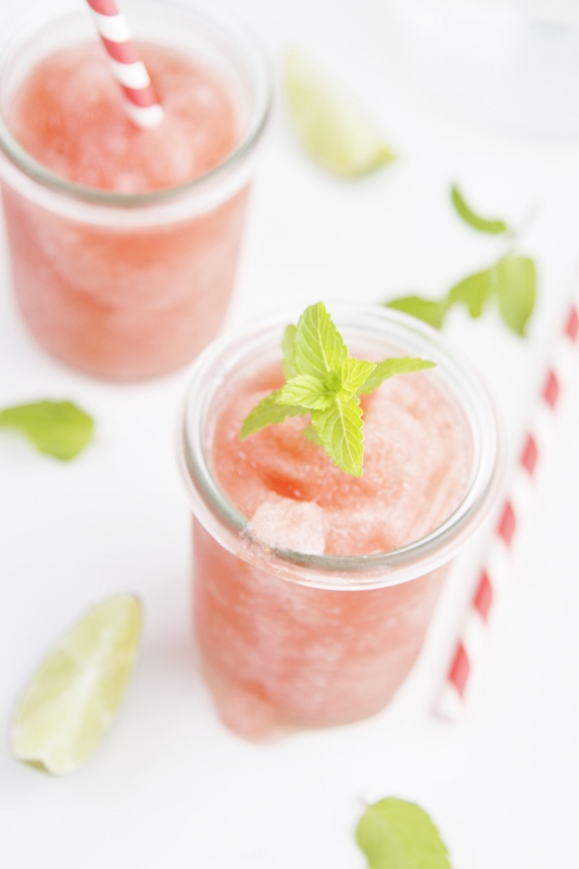 Two glasses of Skinny Strawberry Daiquiris garnished with fresh mint. Striped straws to side.