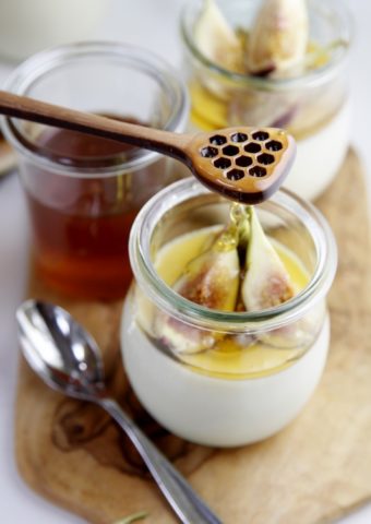 panna cotta in small glass jar topped with figs. Honey drizzling onto panna cotta from above