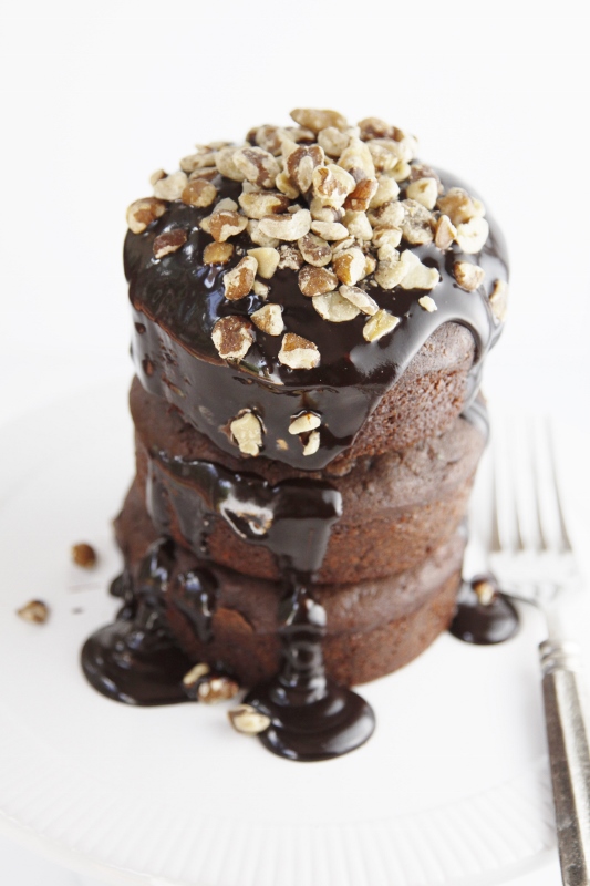 stack of 3 mini chocolate zucchini cakes. Drizzled with chocolate glaze and nuts. Fork to side. 