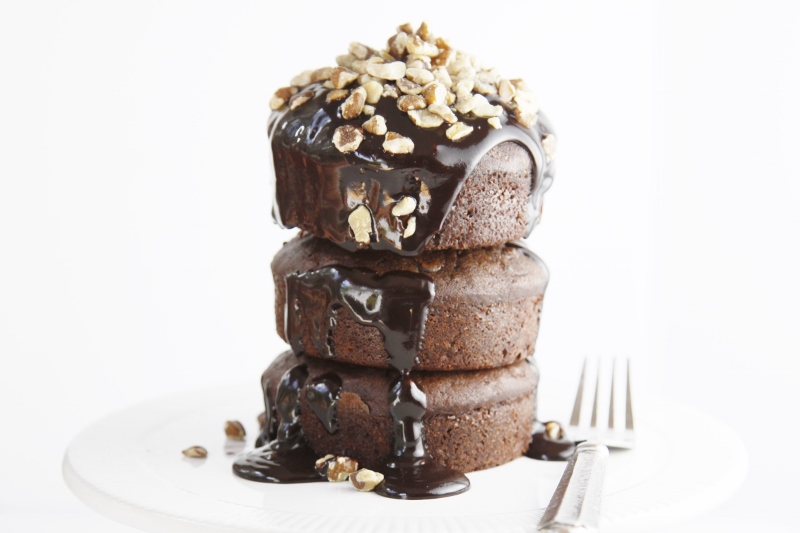 Stack of 3 Death by Chocolate Zucchini Cakes on white plate. Chocolate glaze dripping off with nuts on top.