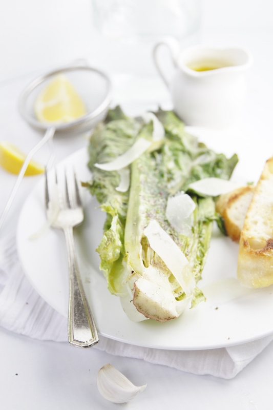 Grilled Caesar Salad on white plate with fork. Lemon wedges and salad dressing in background.