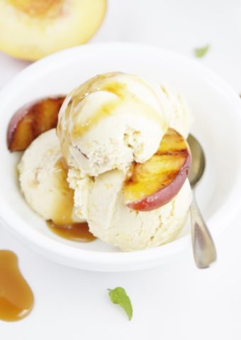 Grilled Peach Ice Cream with Caramel Sauce in white bowl with spoon. Peach in background.