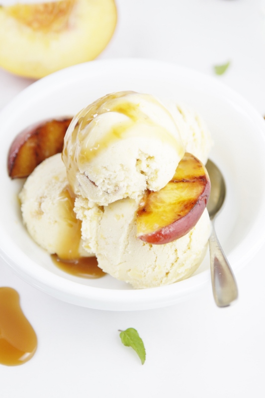 Grilled Peach Ice Cream with caramel sauce in a white bowl with spoon. Peach in background.