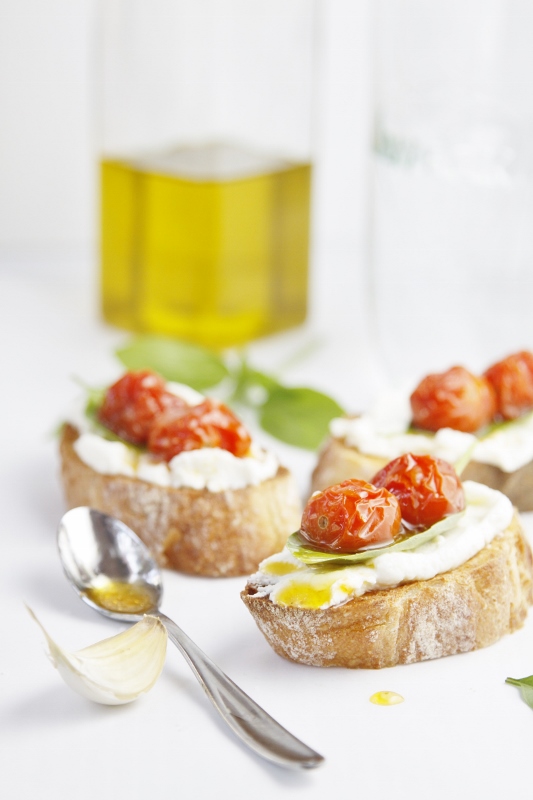 Roasted Tomato and Ricotta Crostini scattered. Bottle of olive oil in background. 