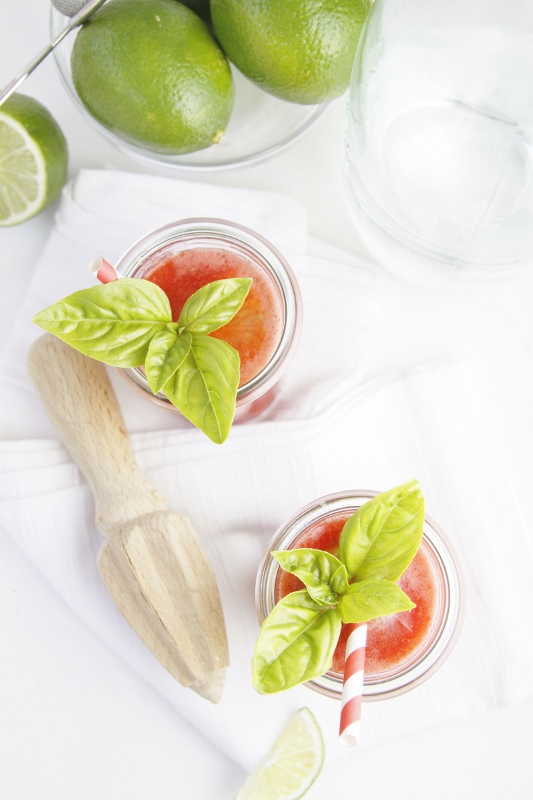 Strawberry Basil Agua Fresca in 2 jars. Limes and citrus juicer to sides. 
