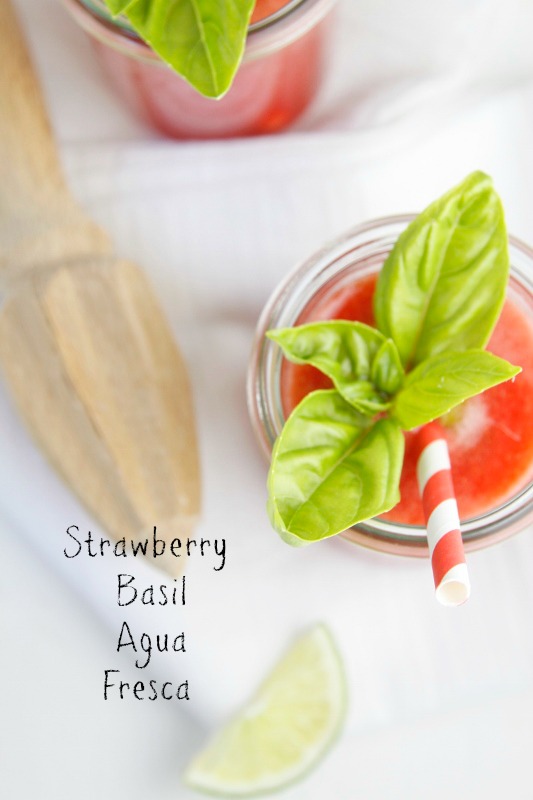 Close up of Strawberry Basil Agua Fresca with straw. Citrus juicer to side. 