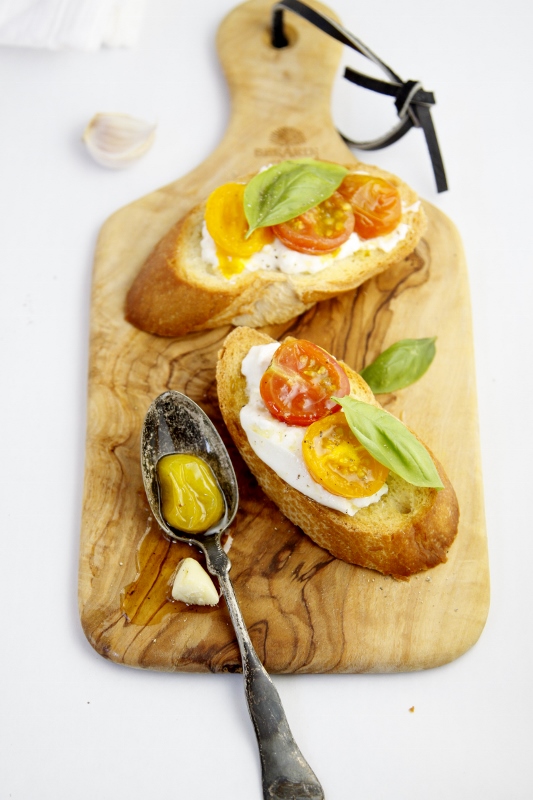 Burrata with Roasted Heirloom tomatoes crostini on small wood cutting board with spoon.