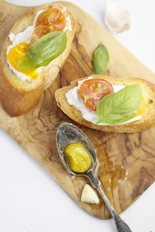 Burrata Crostini with Roasted Heirloom Tomatoes on small wood cutting board with spoon.