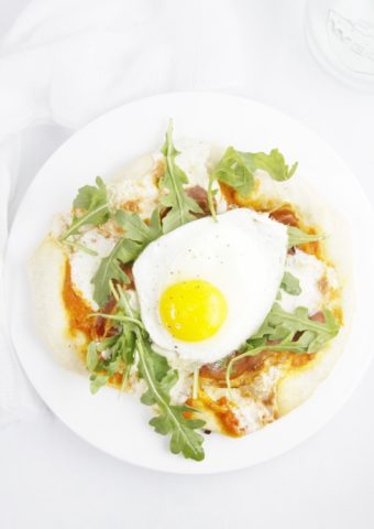 Prosciutto Arugula and Fried Egg Pizza on white plate with fork.