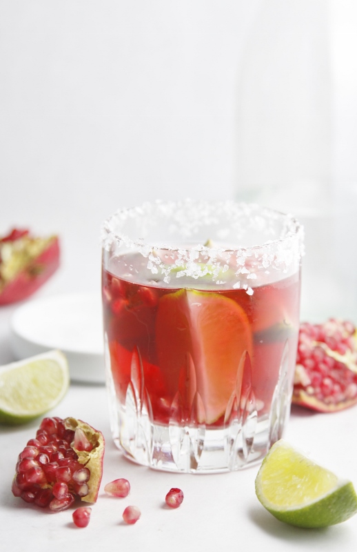 Pomegranate Lime Margarita with lime wedges and pomegranates scattered around.