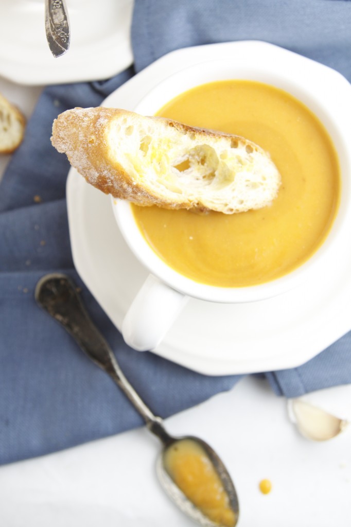 Creamy Roasted Pumpkin Soup in white cup with baguette slice.