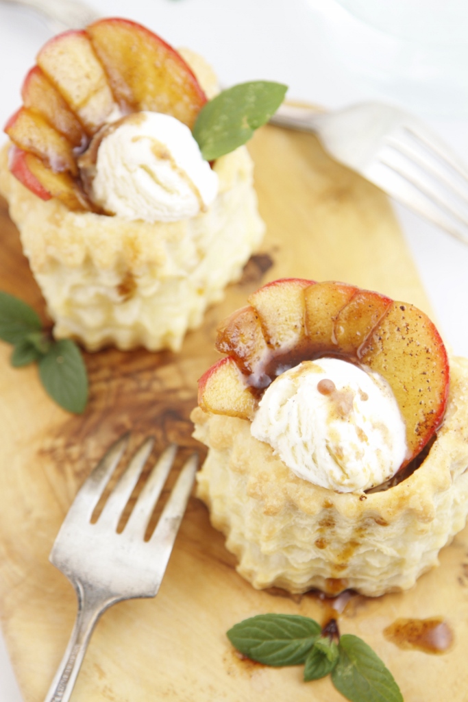Two Puff Pastry Cups filled with apples, ice cream sitting on a cutting board. Forks to side. 