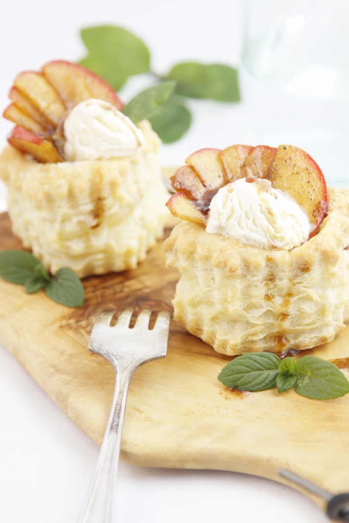 Two Puff Pastry Cups filled with apple slices and ice cream sitting on a cutting board. Fork in front and mint leaves. 