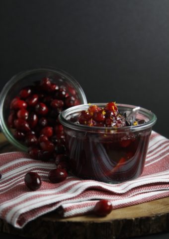 glass jar of cranberry chutney on kitchen towel, glass jar of cranberries on side.
